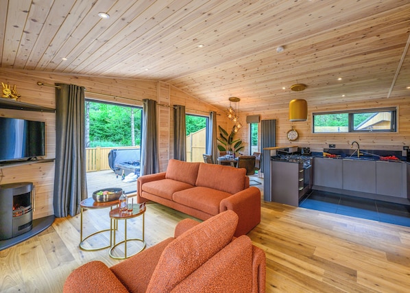 A modern cabin interior with a wooden ceiling, a sofa, a TV, a kitchen, and a dining area.