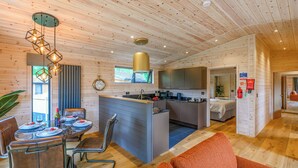Un interior moderno con comedor, cocina y sala de estar, que destaca por sus techos de madera y muebles contemporáneos.