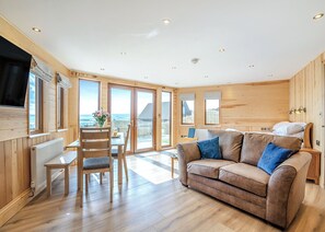 A cozy room with a sofa, a dining table, and a chair. There are large windows and a view of the outside. - 1 bedroom accommodation in Ripponden (Ripponden)