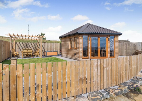 Una cabaña de madera con patio trasero cercado, pérgola y jacuzzi.