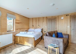 A wooden-paneled room with a bed, a sofa, a small table with magazines, and a window with a view. - 1 bedroom accommodation in Ripponden (Ripponden)