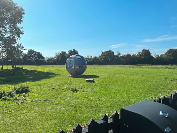 Una estructura esférica en un campo cubierto de hierba, con árboles al fondo.