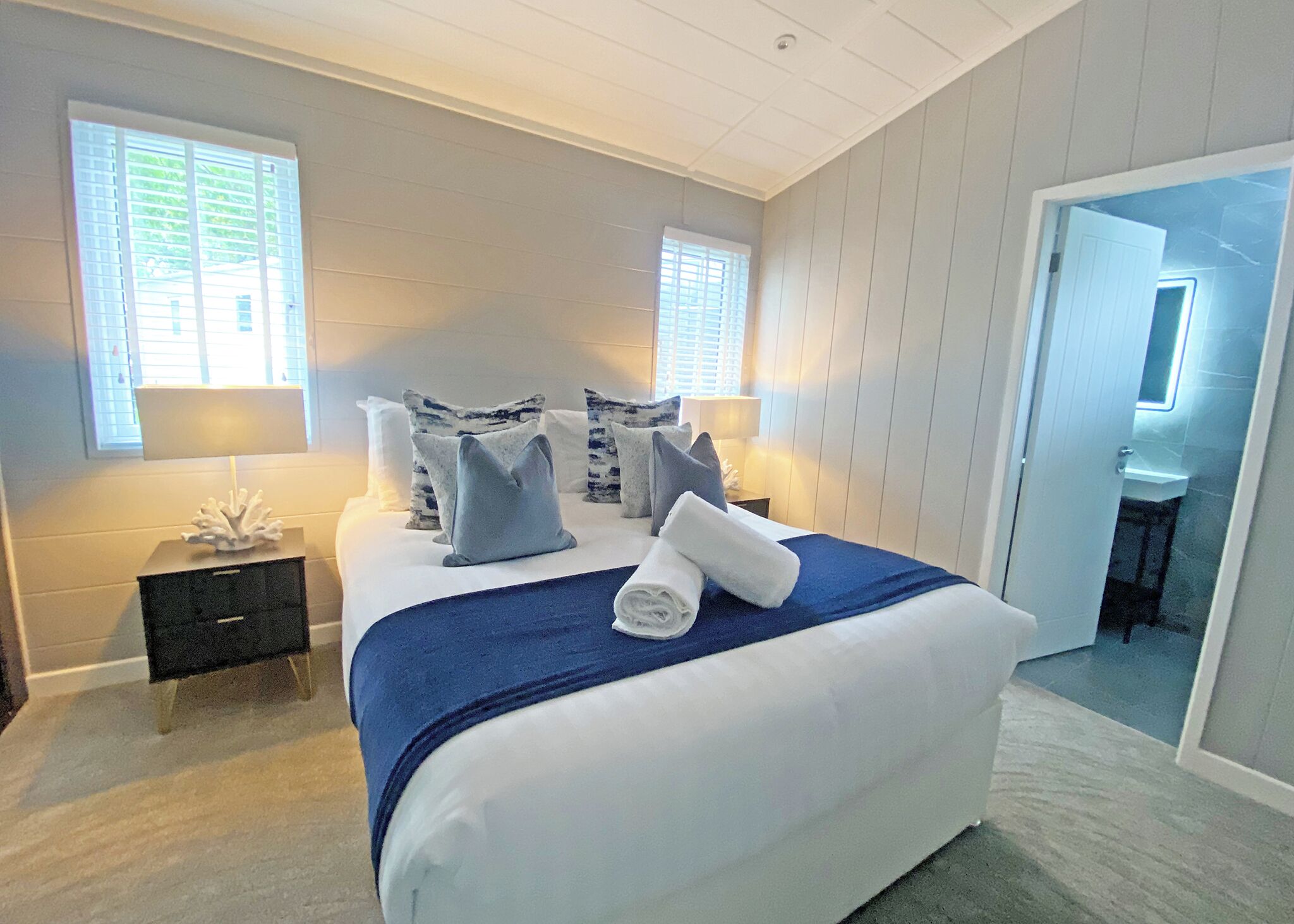 A bedroom with a large bed, two bedside tables, a nightstand, and a bathroom visible through an open door.