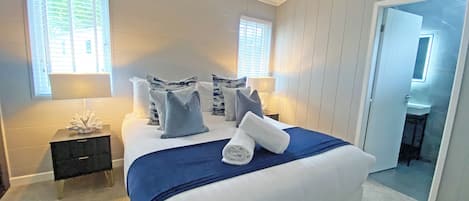 A bedroom with a large bed, two bedside tables, a nightstand, and a bathroom visible through an open door.