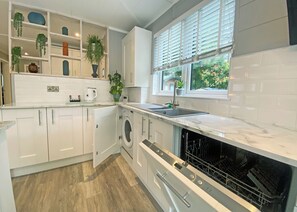 Een moderne keuken met witte kastjes, een ingebouwde wasmachine, een vaatwasser en een raam met zonwering.
