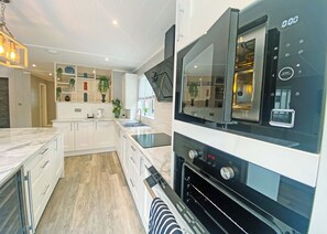 A modern kitchen with white cabinetry, a built-in oven, and a large window. - Super spacious modern lodge with large balcony and hot tub. (Snowdonia)