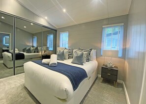 A modern bedroom with a large bed, a mirror, a nightstand, and a window with blinds. - Super spacious modern lodge with large balcony and hot tub. (Snowdonia)