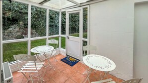 Un patio cubierto con dos mesas redondas y cuatro sillas, un calentador pequeño y una puerta que da al exterior.