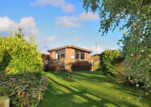 A wooden house with a fenced yard, surrounded by greenery.