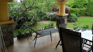 Een terras buiten, met een stenen zuil, een metalen stoel en een tafel.