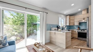 A modern kitchen with a central island, wooden cabinets, and a large window overlooking a garden. - Blanchet Casita – Stylish 1BR Casita w/ Fire Pit & Patio (Vancouver)