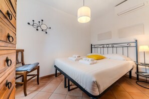 Quarto com cama, mesas de cabeceira, uma cadeira, uma obra de arte na parede e um candeeiro suspenso.