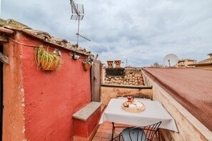 Um edifício vermelho com uma mesa e cadeiras brancas, uma antena parabólica e uma pequena área de jardim.