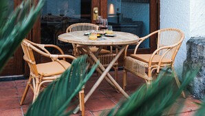 A round table with wicker chairs and a glass top, surrounded by a stone wall and a wooden door. - Casa d'Abreu Neto - Siza's First Work (Matosinhos)