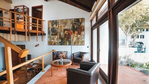 A spacious interior with a wooden staircase, a large abstract painting, and a view of the street outside. - Casa d'Abreu Neto - Siza's First Work (Matosinhos)