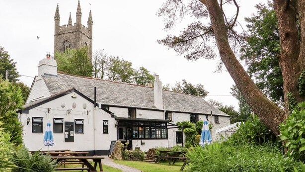 A traditional white building with a stone tower in the background, a paved pathway, and a picnic table in the foreground. - Lannlyvri Lodge (Bodmin)