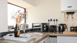 A modern kitchen with a built-in island, a wine bottle, a glass, a toaster, a kettle, and a book on the counter. - Lannlyvri Lodge (Bodmin)