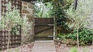 A garden pathway leading to a wooden gate, surrounded by potted plants and a stone wall. - Camellia Cottage (Bodmin)