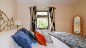 A bedroom with a bed, a window with curtains, a bedside lamp, and a mirror. - Camellia Cottage (Bodmin)