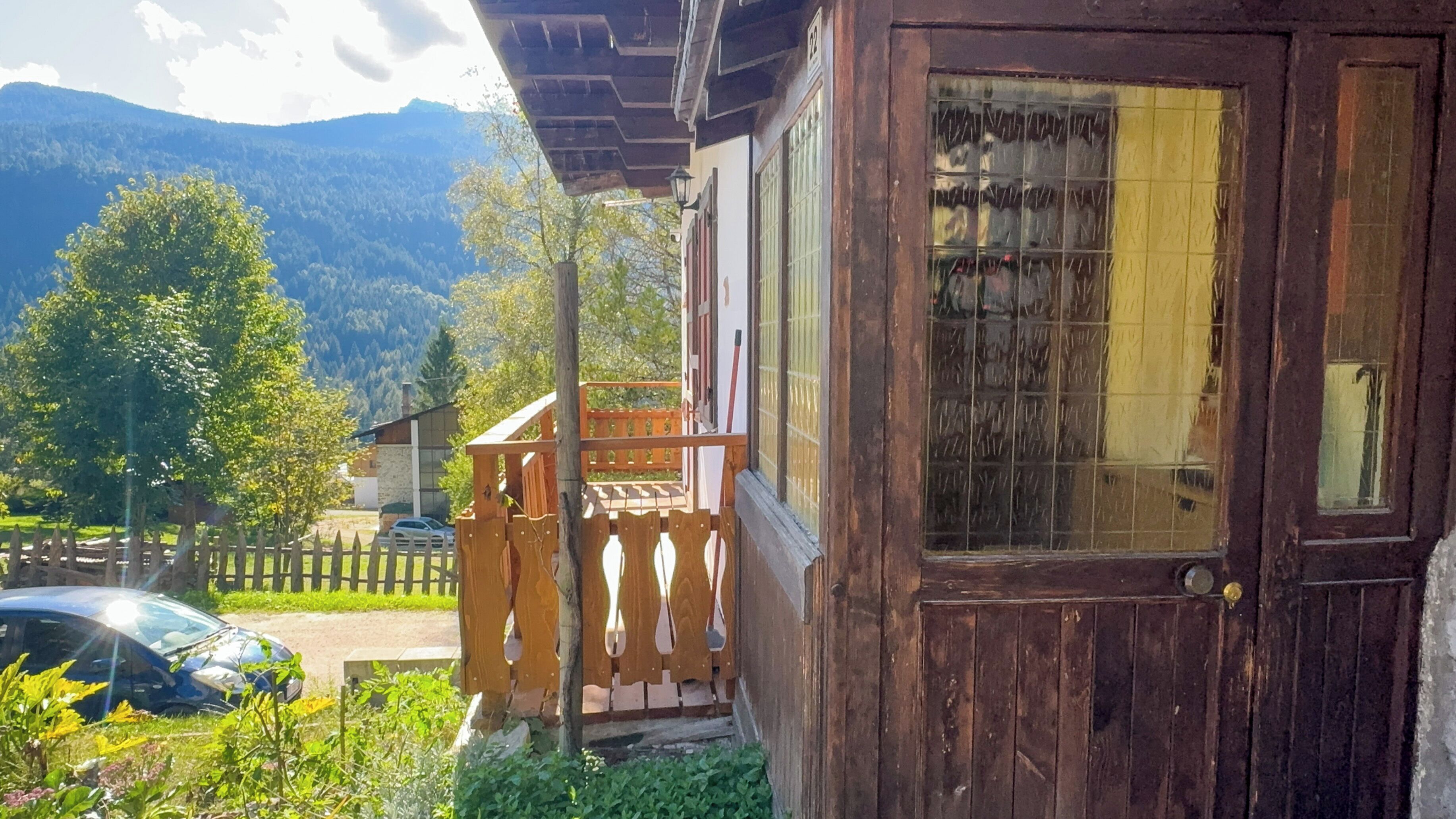 Et træhus med balkon, bil foran og bjerge i baggrunden.