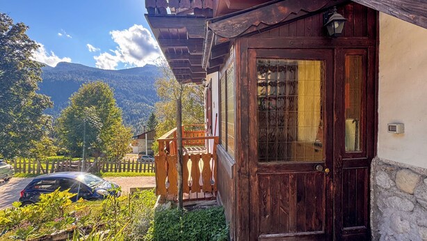 Una casa tradizionale in legno con veranda in legno, una porta in vetro e vista su una catena montuosa.