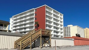 Ein mehrgeschossiges Hotel mit roter und weißer Fassade, einer Holztreppe und sandigem Untergrund.