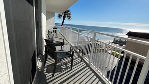 Ein Balkon mit Blick auf das Meer, einer Palme und einem Tisch mit Stühlen.