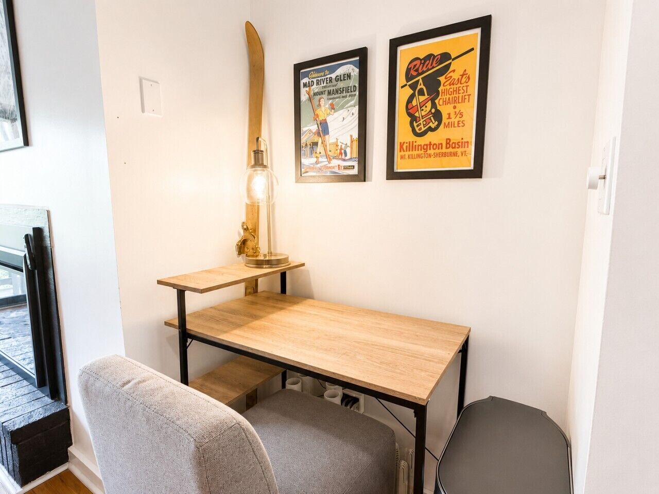 Une pièce comprenant un bureau en bois, une chaise, une lampe et deux affiches encadrées accrochées au mur.