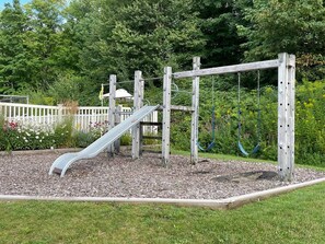 Une aire de jeux avec un toboggan, des balançoires et une structure d’escalade en bois.