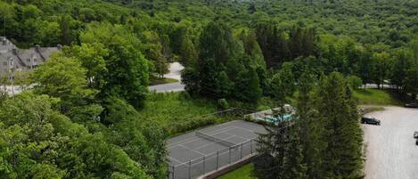 Een tennisbaan omringd door dicht bos en een berg op de achtergrond.