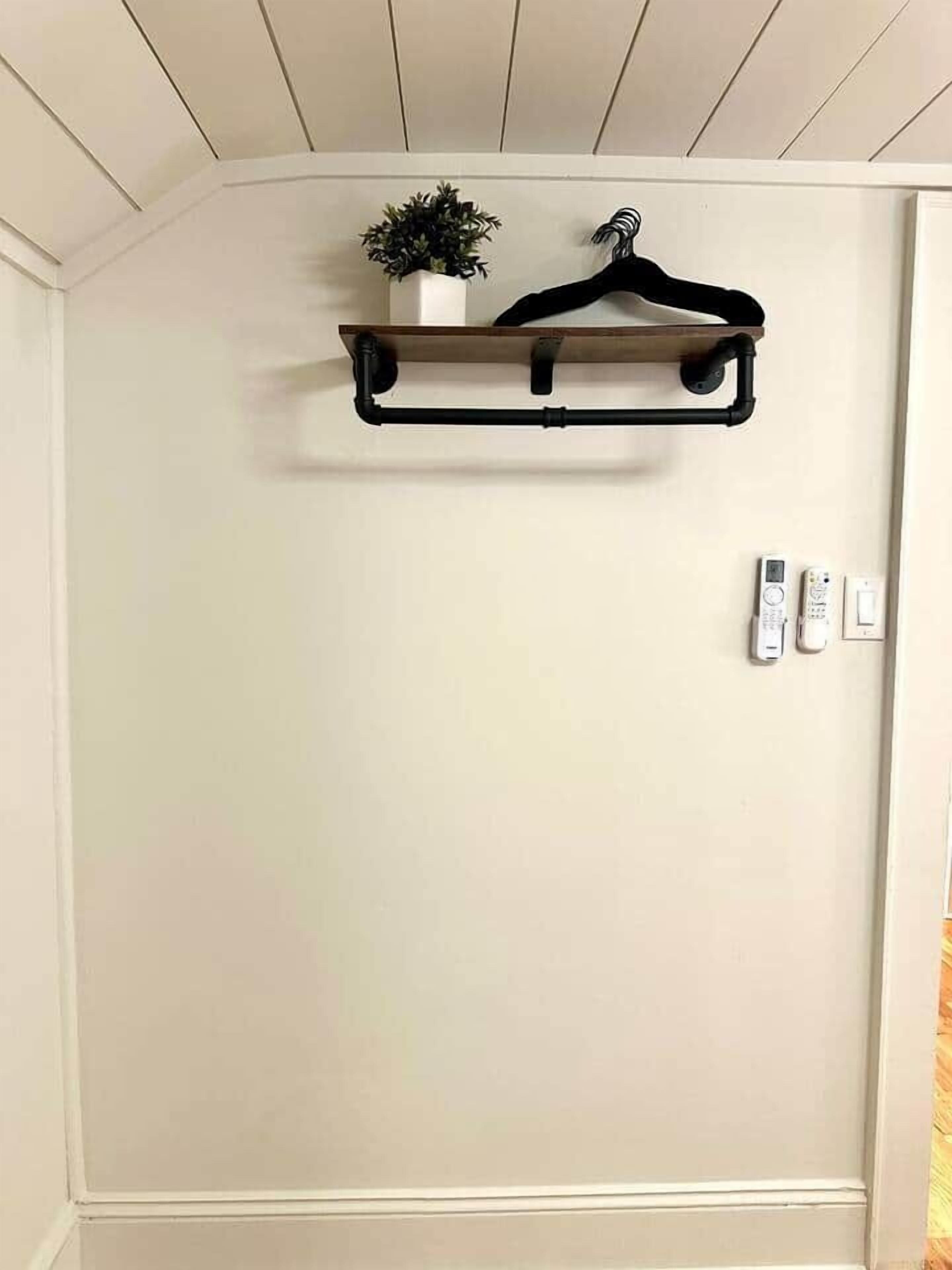 Een hoekmuur met een zwarte metalen plank waarop een potplant en een zwarte kapstok staan. Aan de rechterkant zitten twee stopcontacten en een thermostaat.