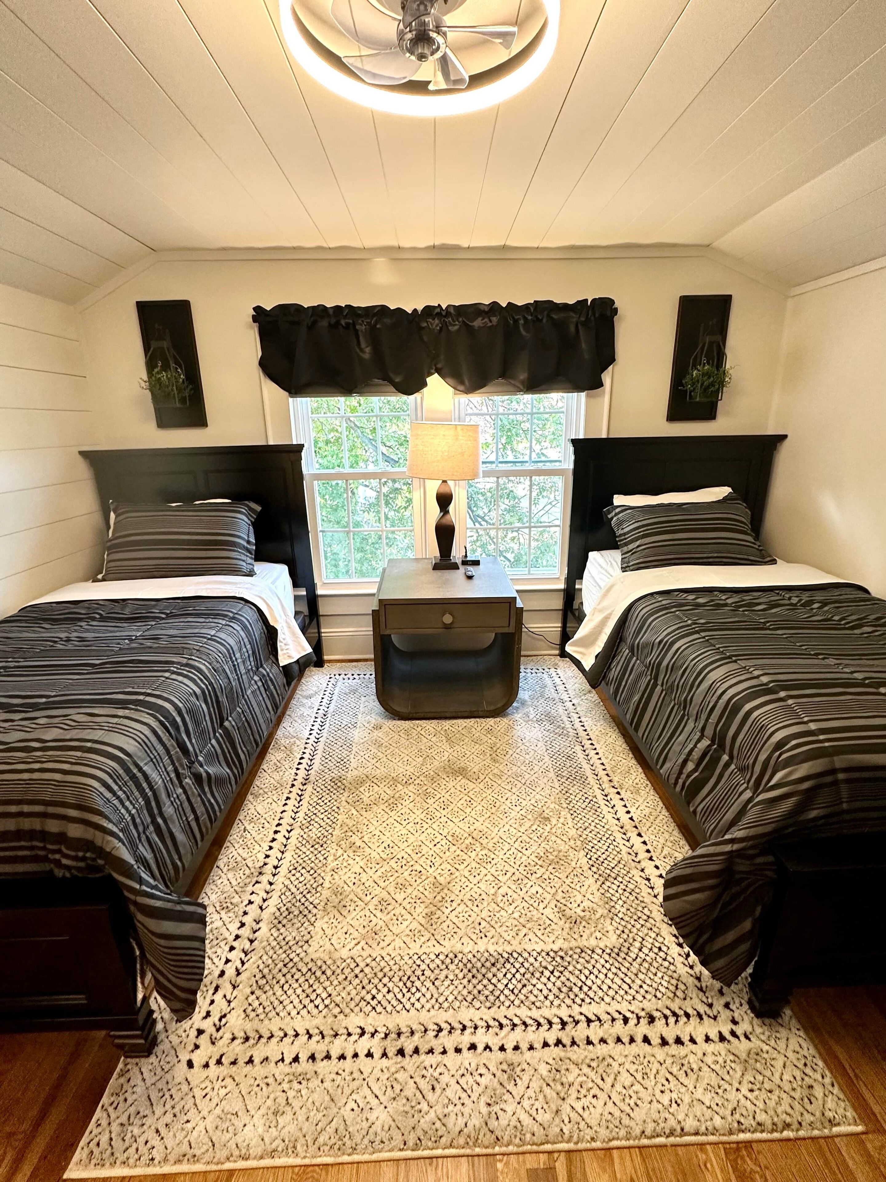 A bedroom with two beds, a nightstand, a lamp, and a window with curtains.