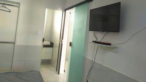 A bedroom with a bed, a television mounted on the wall, a door, and a bathroom visible through an open door. - Pousada Sol e Mar Ilhéus (Ilhéus)