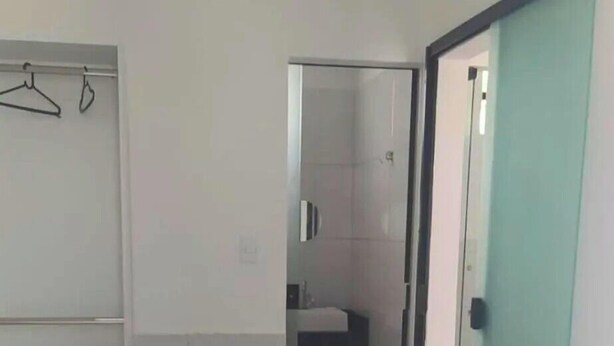 A hotel room with a bed, a bathroom visible through a glass door, and a coat rack. - Pousada Sol e Mar Ilhéus (Ilhéus)