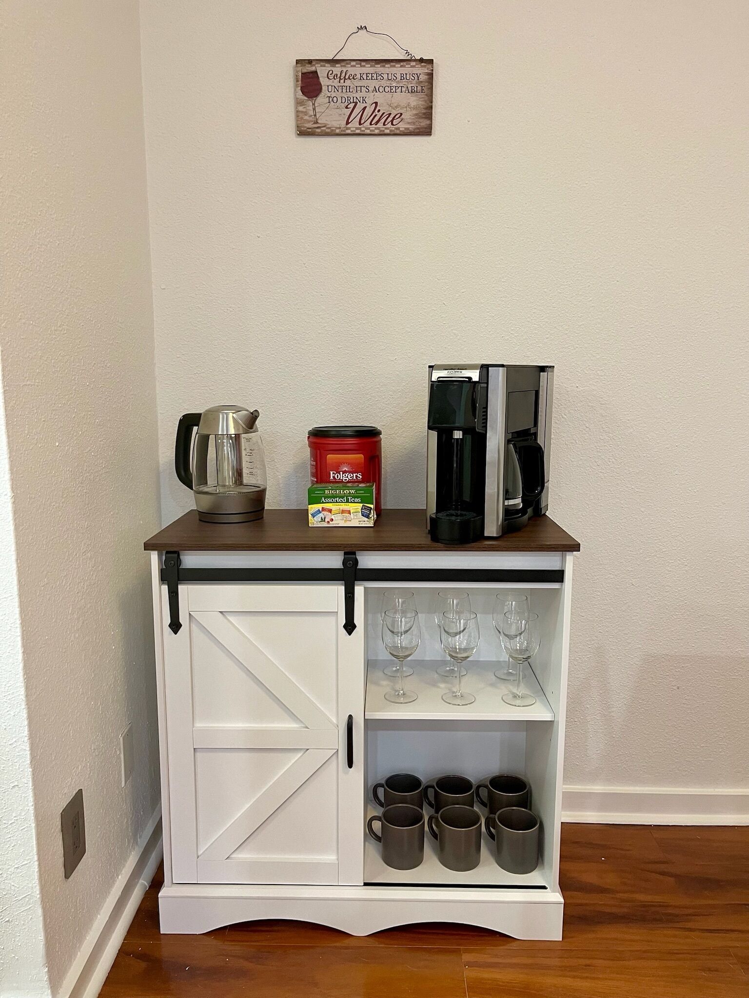 A small white cabinet with a coffee maker, a Folgers coffee can, and wine glasses.
