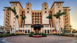Een groot, meerhoog hotel met een centrale ingang, meerdere balkons en palmbomen.