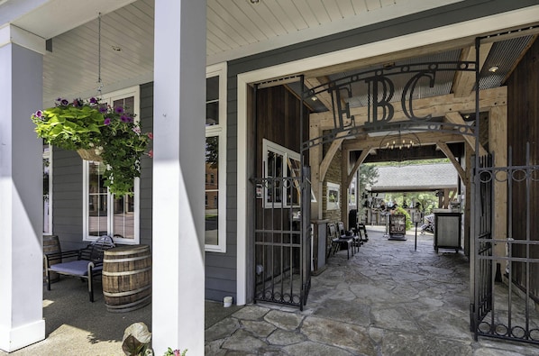 A covered outdoor area with a wooden bench, a hanging flower basket, and a stone pathway leading to a gate with 'BC' above it.
