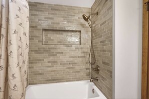 A shower area with a tiled wall, a showerhead, and a curtain with ski patterns.