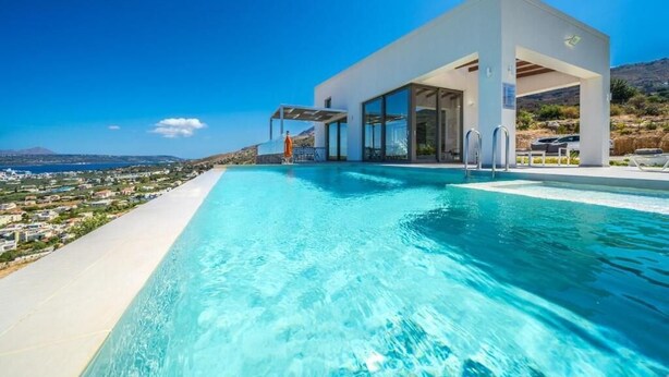 Un área moderna junto a la piscina con vista despejada al mar y un edificio con amplios ventanales.