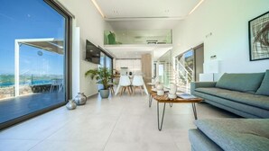 Una sala de estar moderna con sofá, mesa de comedor y sillas, un televisor montado en la pared y un balcón con vistas.