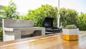 Un área de estar exterior de hormigón con un lavabo, una parrilla y una planta en maceta.