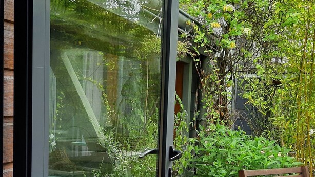 A glass door leading to a patio with a wooden bench, a potted plant, and a small table. - Guest Room “La Musicale - Django Reinhardt” with Breakfast Included (Rouen)