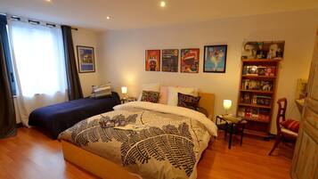 Een tweepersoonsbed met een bedsprei met dessin, een nachtkastje met lamp, een boekenkast en een raam met gordijnen.