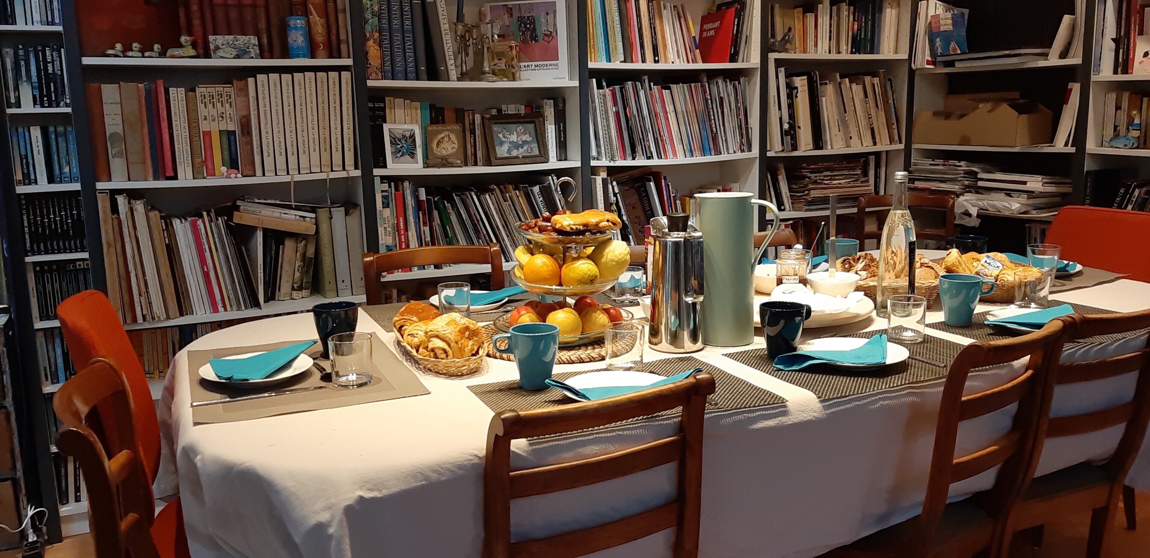 Une table à manger dressée avec de la nourriture et des boissons, entourée d’étagères remplies de livres.
