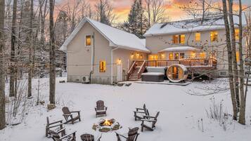 A two-story house with a deck and a fire pit in the snow.