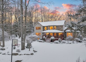 Ein zweigeschossiges Haus in verschneiter Landschaft, umgeben von Bäumen.