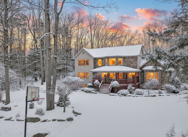 A two-story house with a snow-covered landscape, surrounded by trees. - Indoor Swim Spa, Barrel Sauna, Hot Tub, Home Theater, Karaoke Lounge & Game Room (Blakeslee)