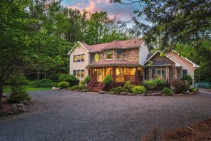 A two-story house with a stone facade, a front porch, and a gravel driveway.