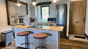 A kitchen with a central island, bar stools, a stainless steel refrigerator, and a wooden door. - Holiday Home 'La P'tite Maiz' with Shared Pool, Private Terrace & Wi-Fi (Bourg-de-Visa)