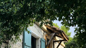 A rustic stone building with a wooden door and blue shutters, a small outdoor seating area with a table and chairs, and a concrete pathway leading to the entrance. - Holiday Home 'La P'tite Maiz' with Shared Pool, Private Terrace & Wi-Fi (Bourg-de-Visa)